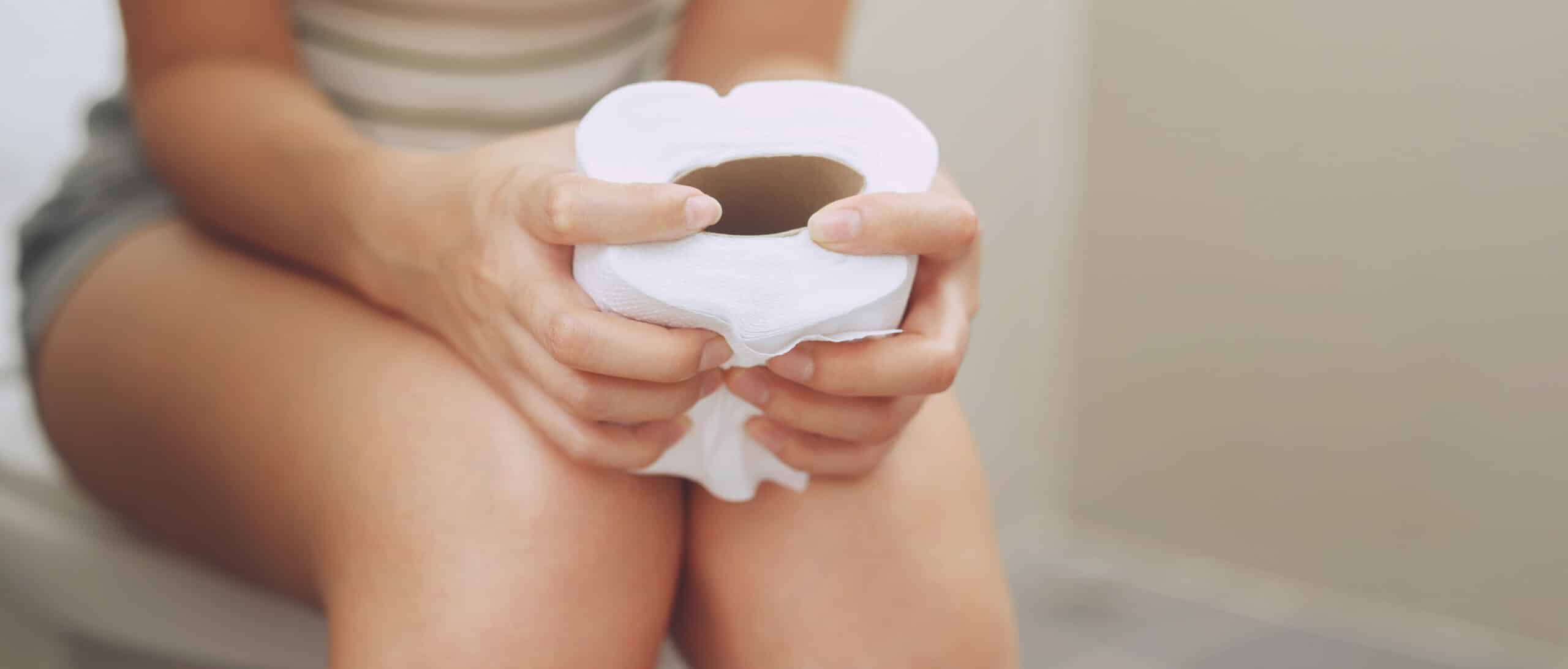 Frau mit Toilettenpapier auf Toilette – Symbolbild für akuten Durchfall.